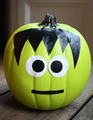 A lime green pumpkin decorated to look like Frankenstein with black hair, googly eyes, and a mouth.