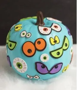 Light blue pumpkin decorated with various googly eyes and monster eyes.