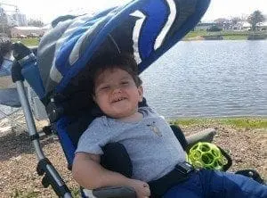 Child in a stroller by a lake smiling.