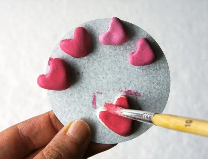 Hand painting small pink clay hearts arranged on a circular gray surface.