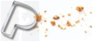 Cookie cutter shaped like the letter P with crumbs scattered next to it.