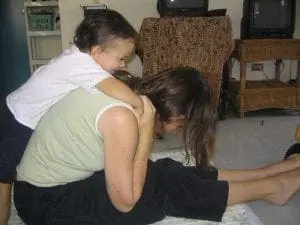 Child sits on woman's back as she lies on the floor.