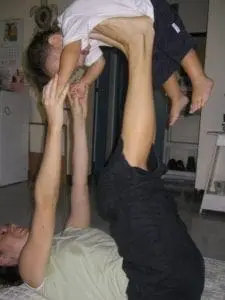 Woman lying on her back, lifting a child in the air with her feet.
