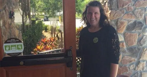 A person wearing a black shirt with decorative sleeves stands in a doorway.