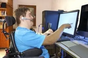 Man in wheelchair pointing at a computer monitor.