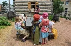Children gathered around a picnic table outside a log cabin.