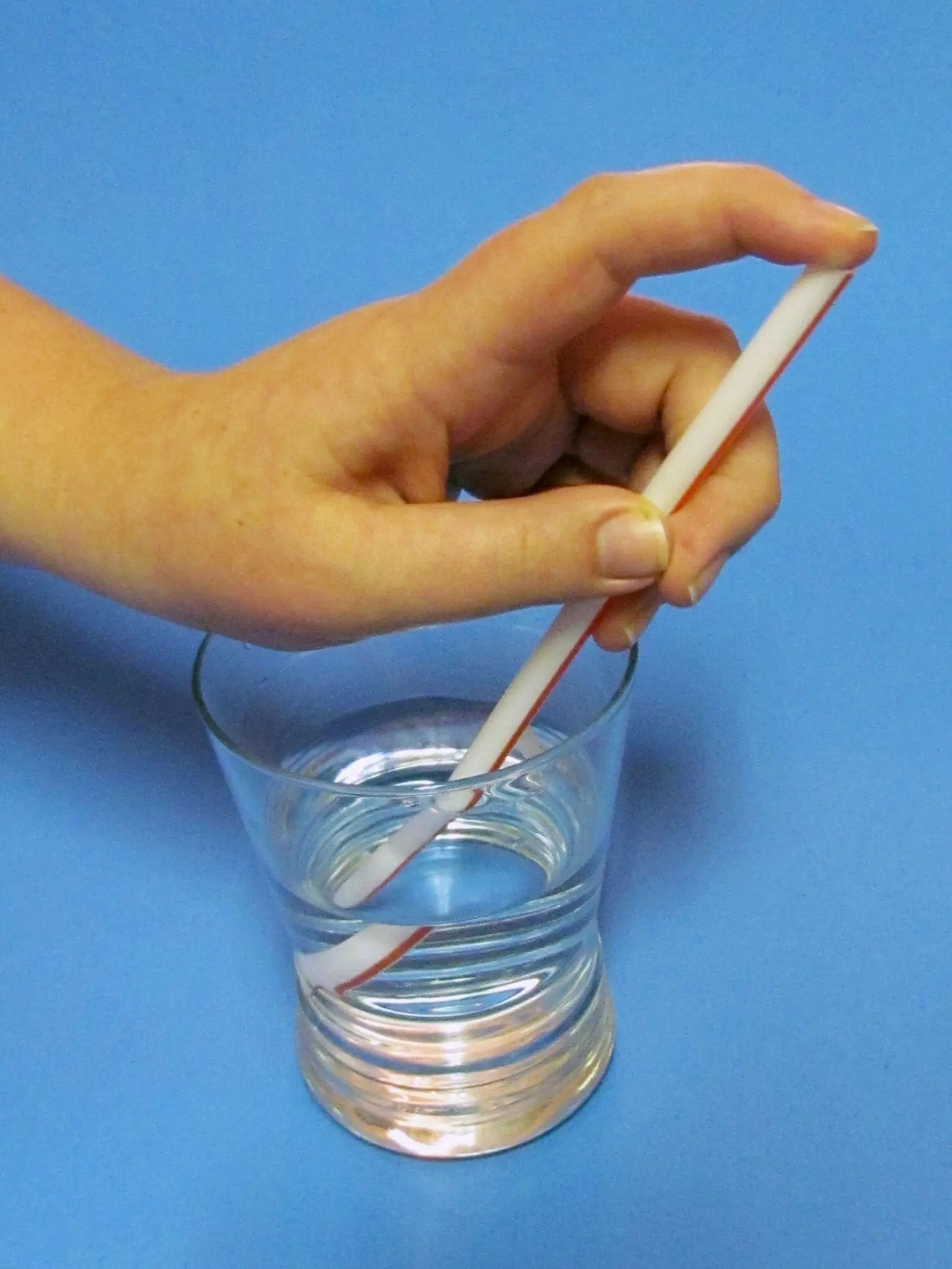 Hand holds a straw over a glass of water to drip onto a pleated straw wrapper.