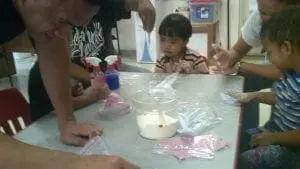 Children and adults gather around a table with craft supplies.
