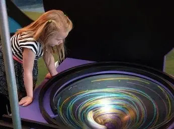 Young girl in striped shirt looking into a vortex exhibit