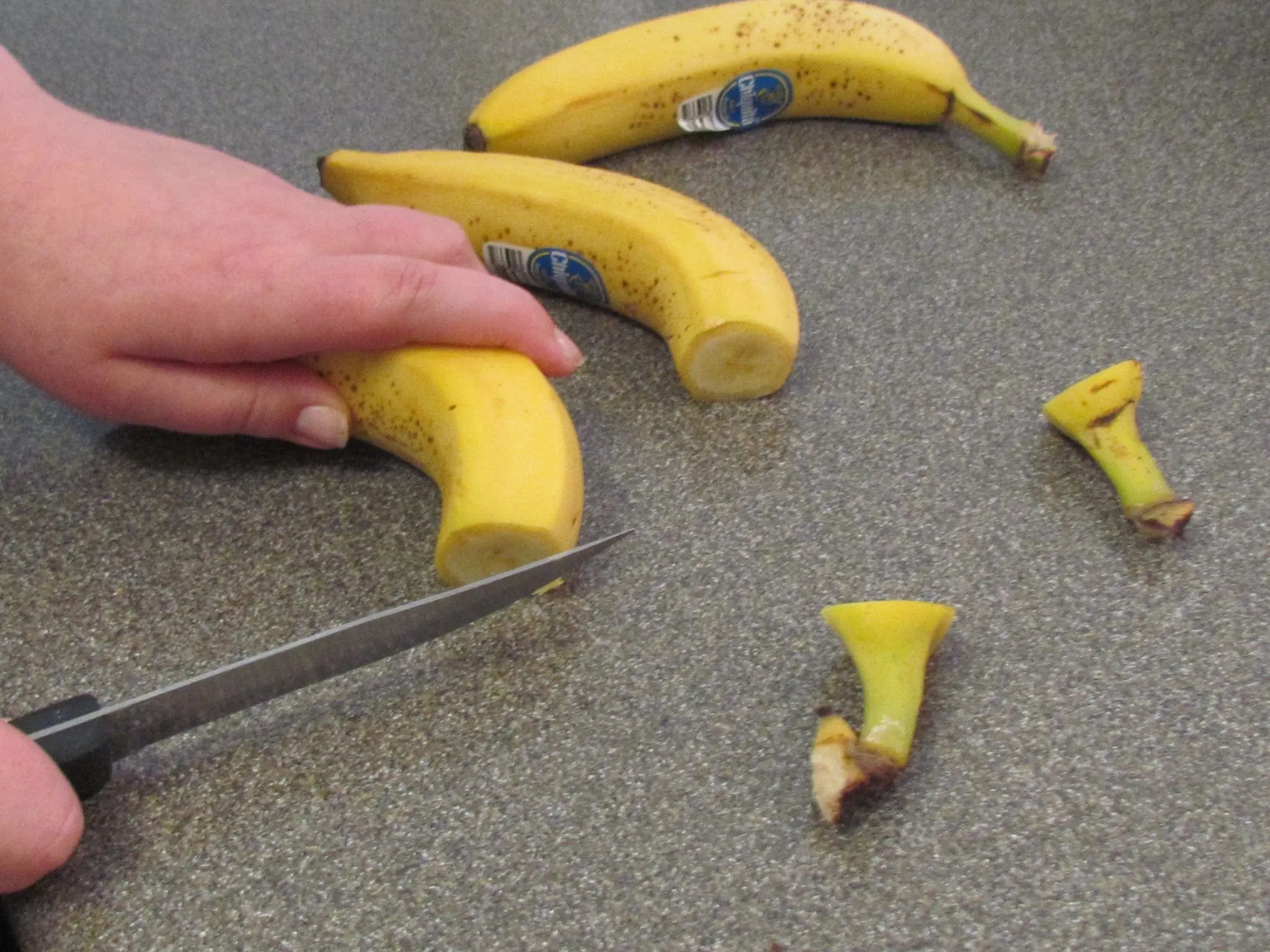 Person slicing the end off a banana with a knife.