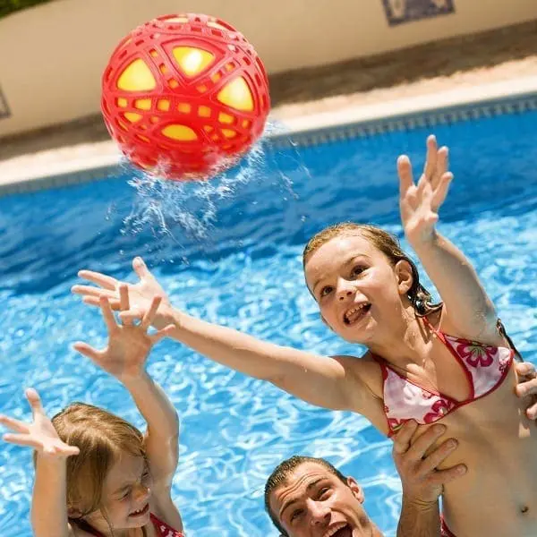 Two children and a man reach for a red ball in a swimming pool.