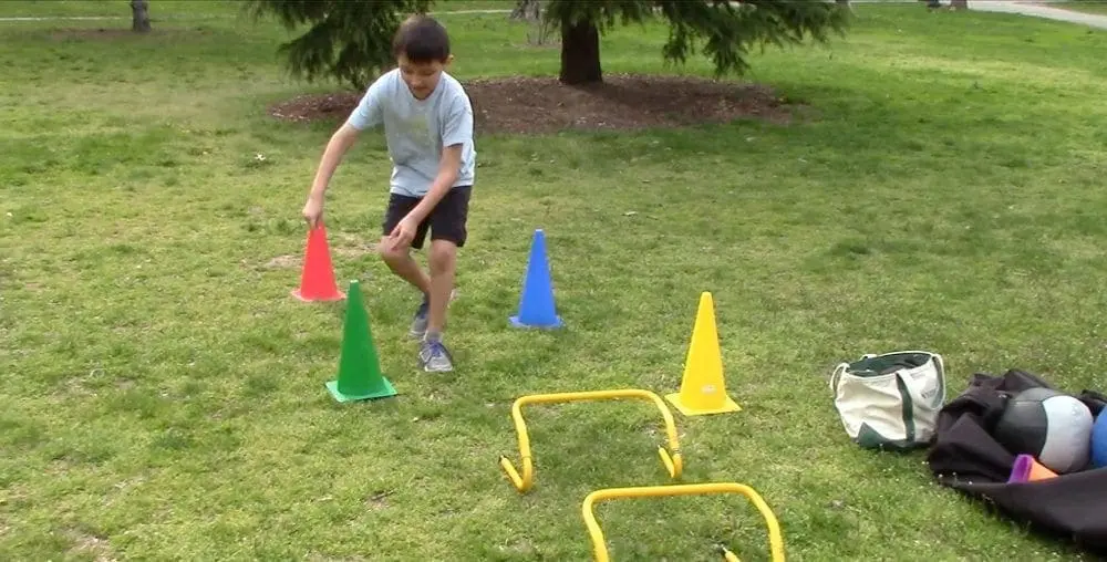 Young person performs cone touches on a grassy field.