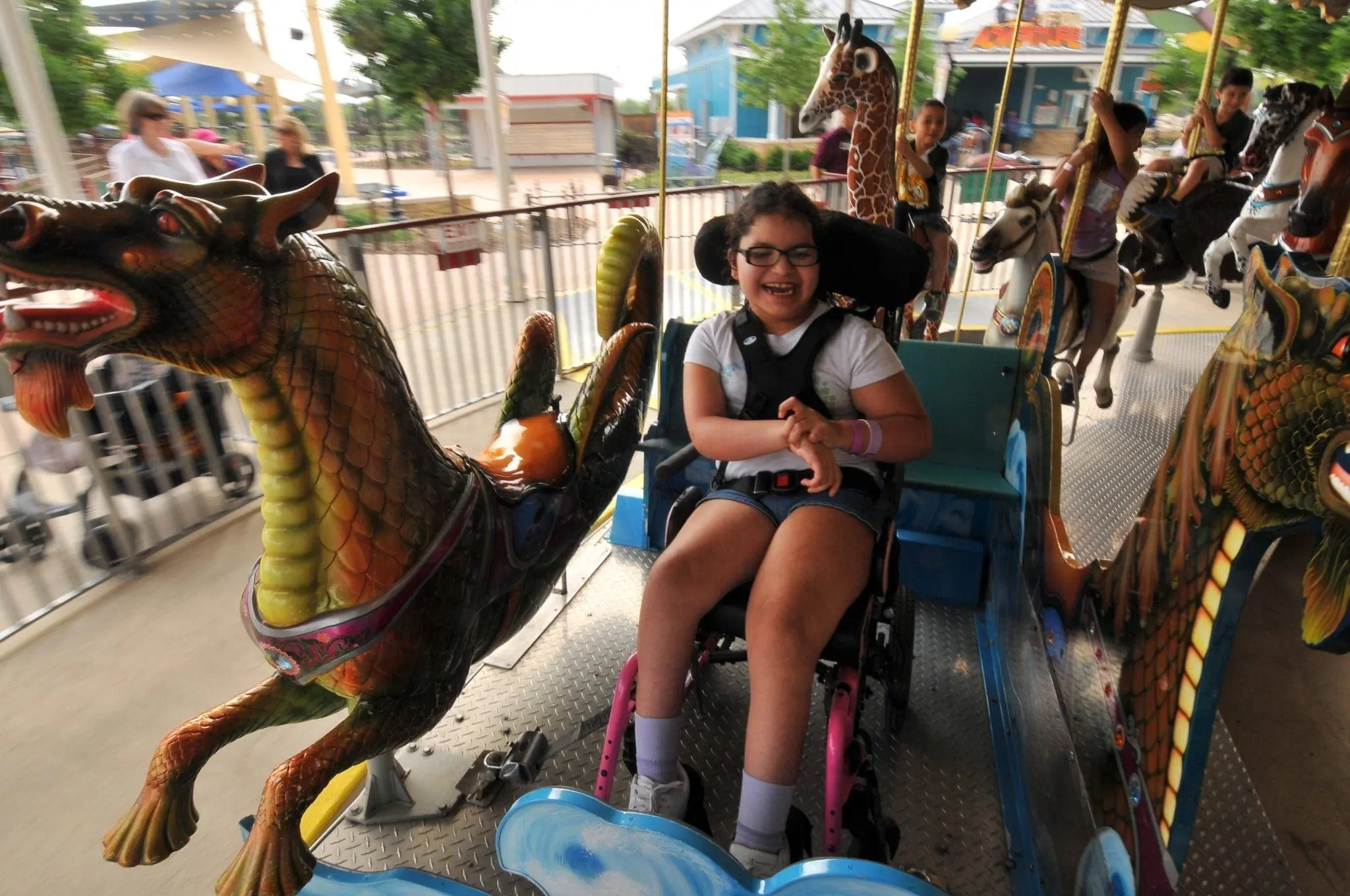 Young girl in a wheelchair smiling on a carousel with dragon and horse figures.