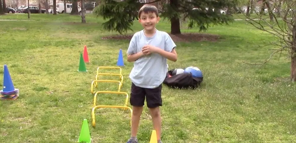 Boy standing in a park with agility hurdles and cones.