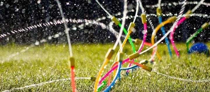 Sprinklers spraying water on a lawn with colorful toys.