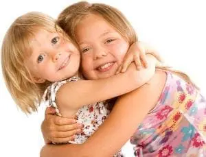 Two young sisters hugging each other and smiling.