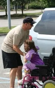 Man helps girl in wheelchair exit a van.