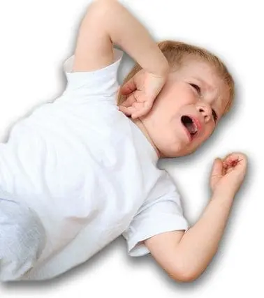 A young child in a white t-shirt cries with their hand over their ear.