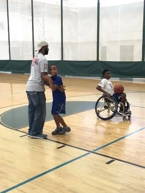 Kelvin Fields coaches a young boy while another boy in a wheelchair holds a basketball.