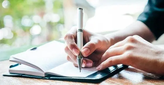 Hands writing in a journal with a pen.