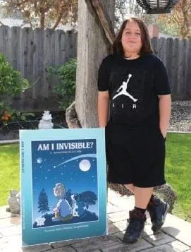 Sam De La Cerda standing next to his book "Am I Invisible?".