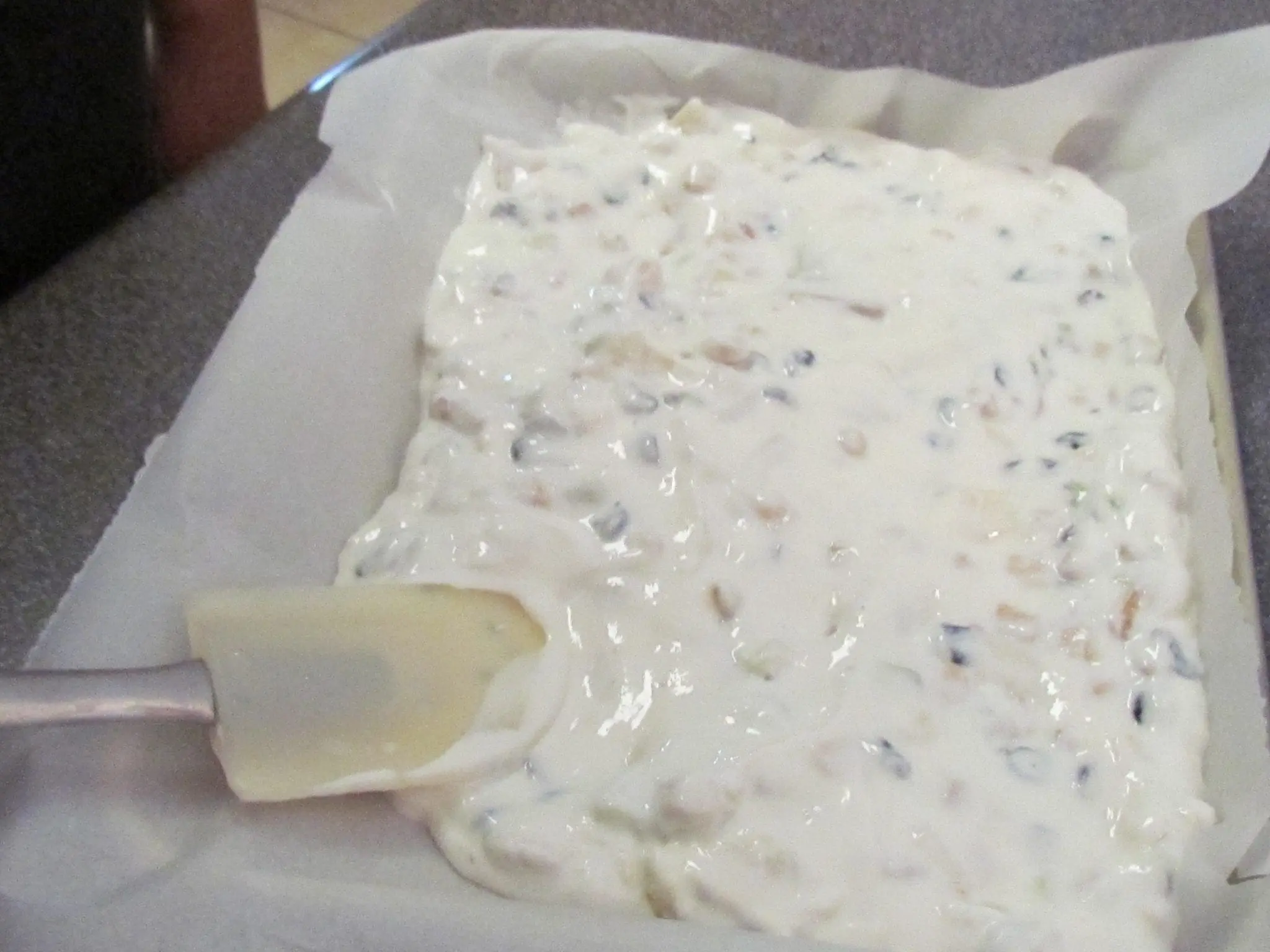 Yogurt mixture being spread onto parchment paper with a spatula