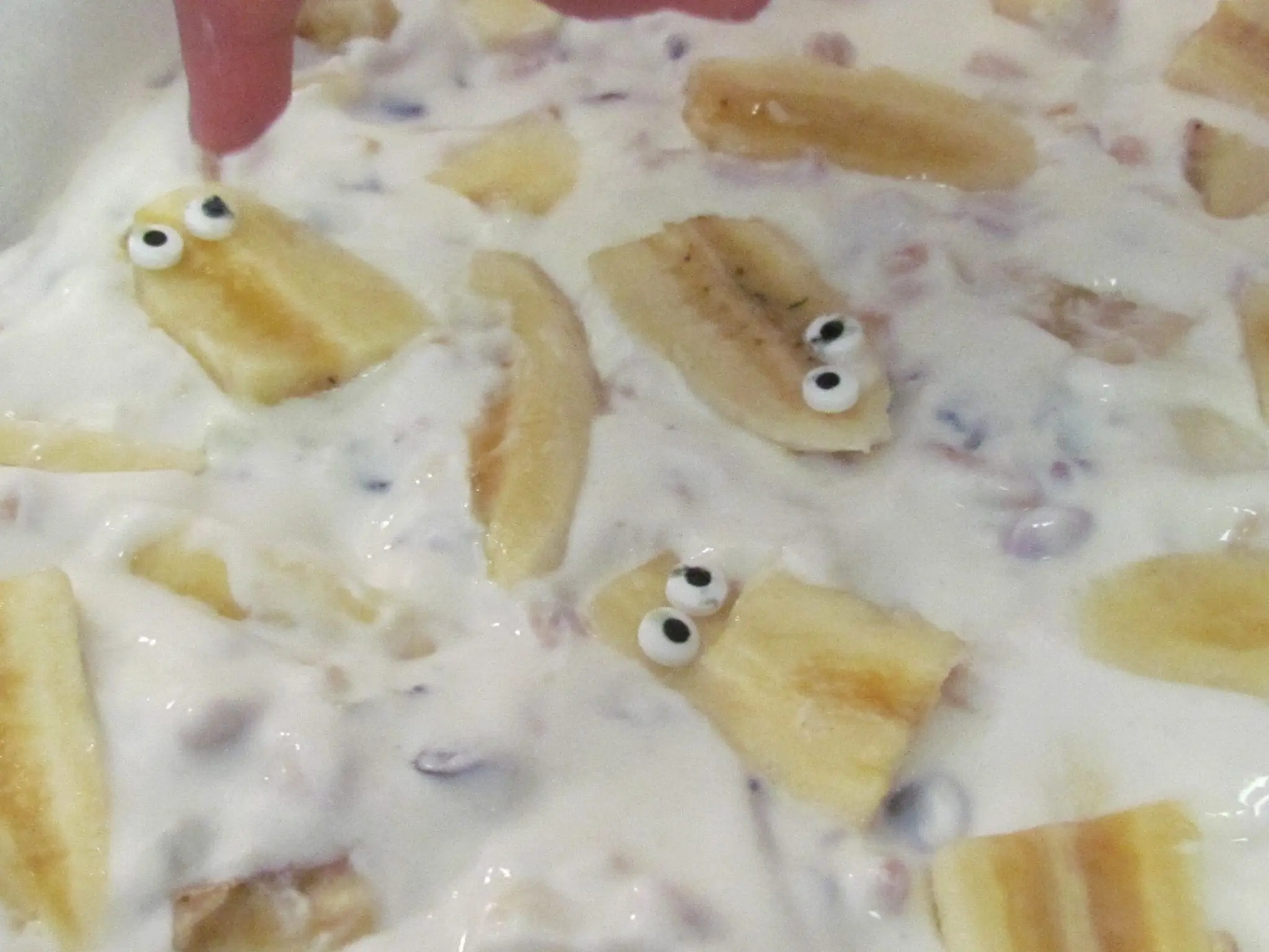 Slices of banana with candy eyes are embedded in a yogurt mixture.
