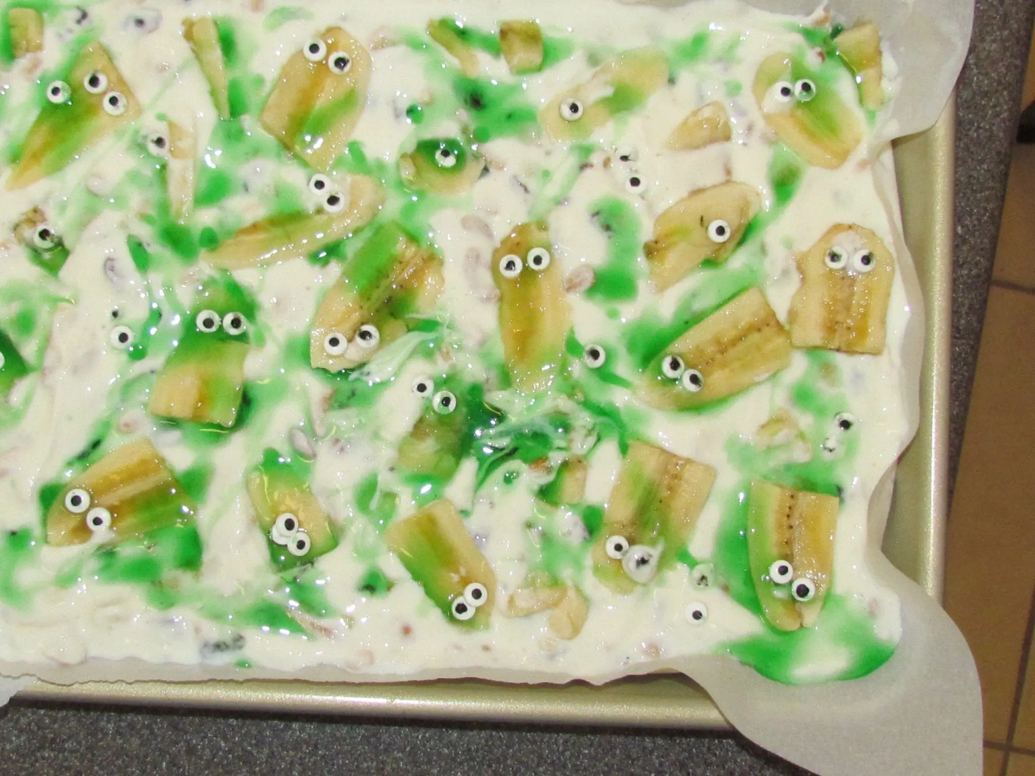 Halloween-themed yogurt bark with banana slices and candy eyes on a baking sheet.