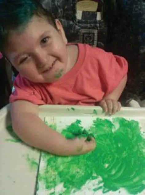 Young child with green paint on their face and hands.