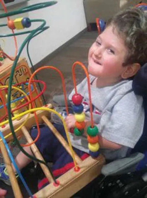 A young child with curly hair smiles while playing with a colorful bead maze toy.