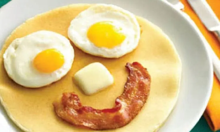 Pancake with two fried eggs, a pat of butter, and a strip of bacon arranged as a smiley face.