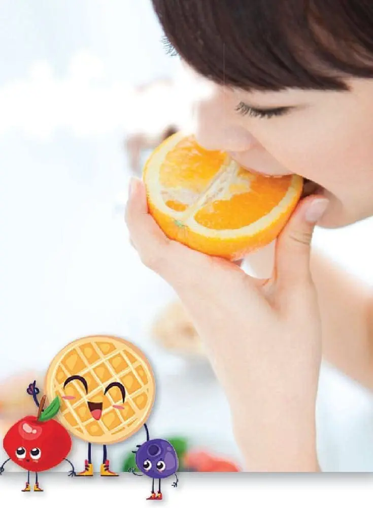 A child eats an orange slice with cartoon fruits and a waffle below.