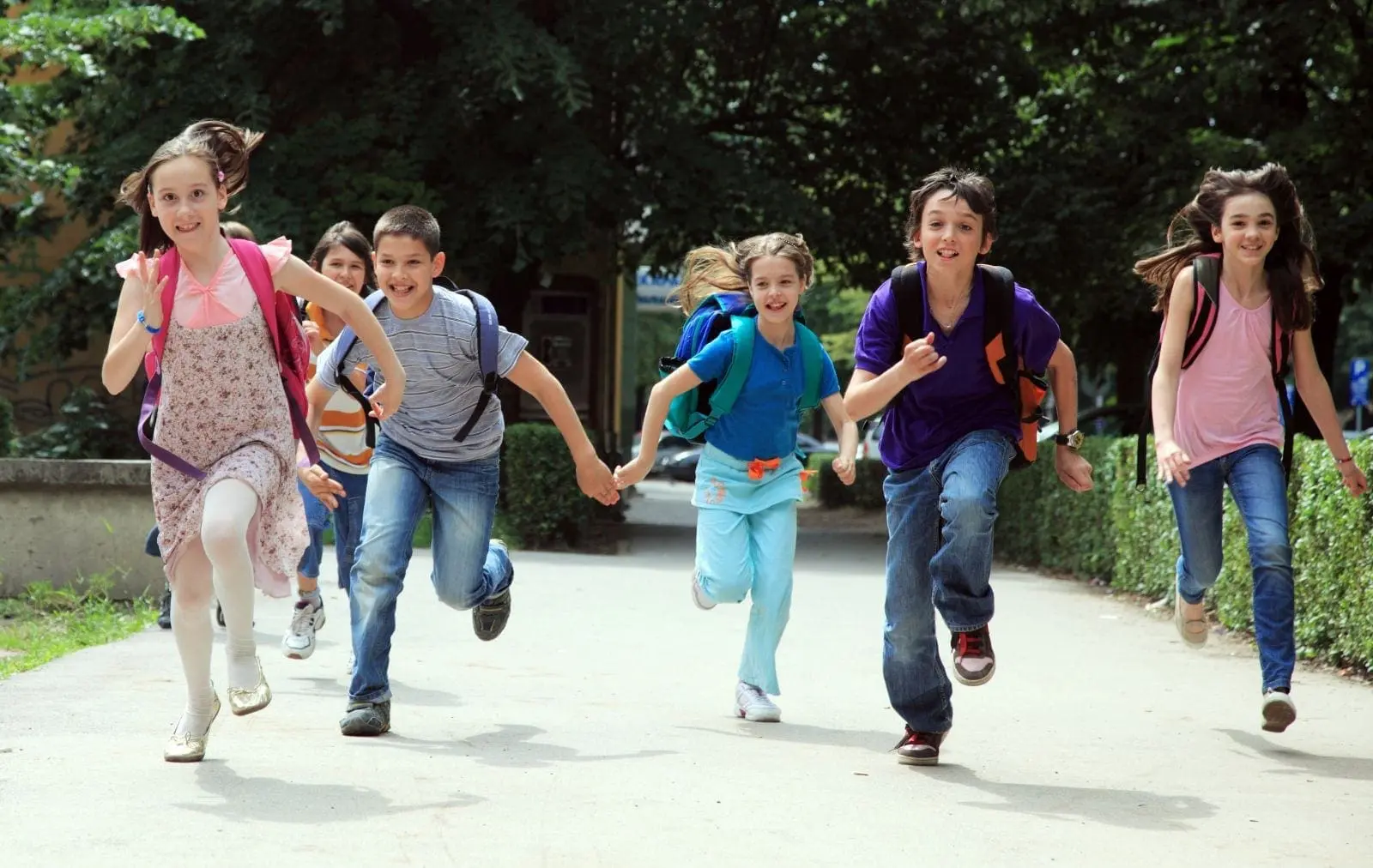 Children with backpacks run along a path toward school.