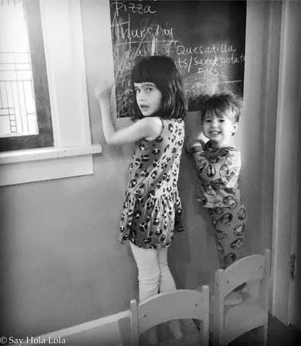 Two children stand by a chalkboard with writing on it.