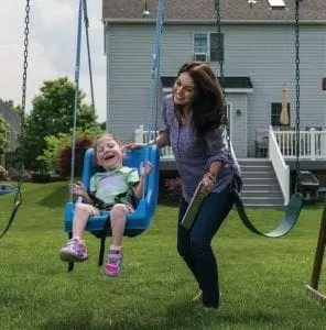 Woman pushing a child on a swing set in a backyard.
