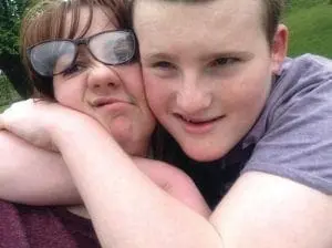 Woman with glasses and a young person embracing.