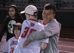 Two young people embrace on a sports field while two others watch.