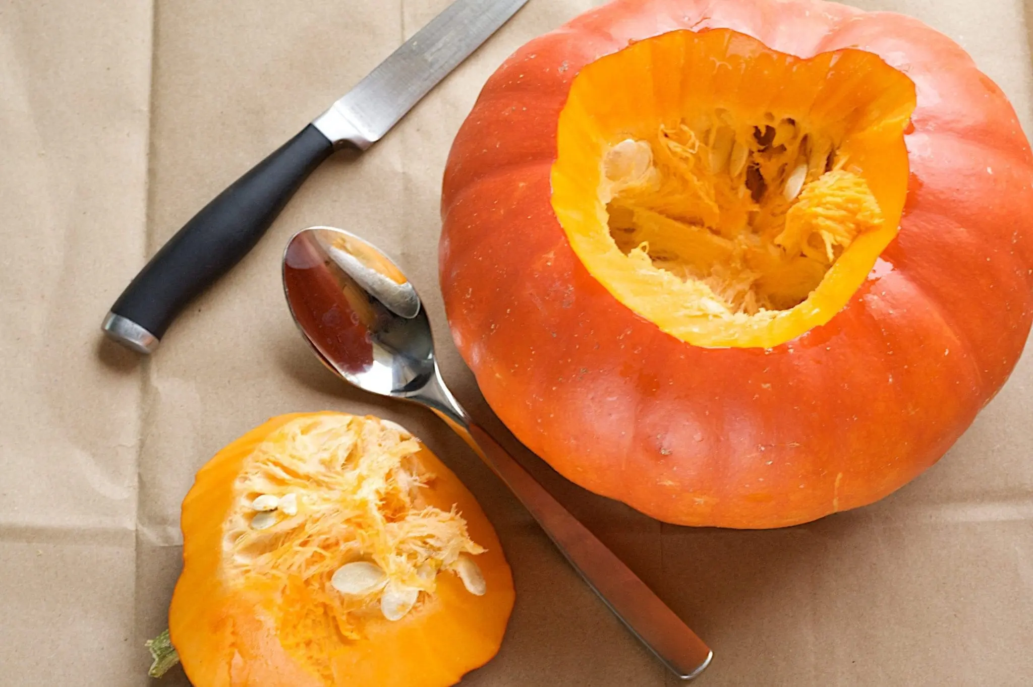 A partially carved pumpkin with a knife and spoon nearby.