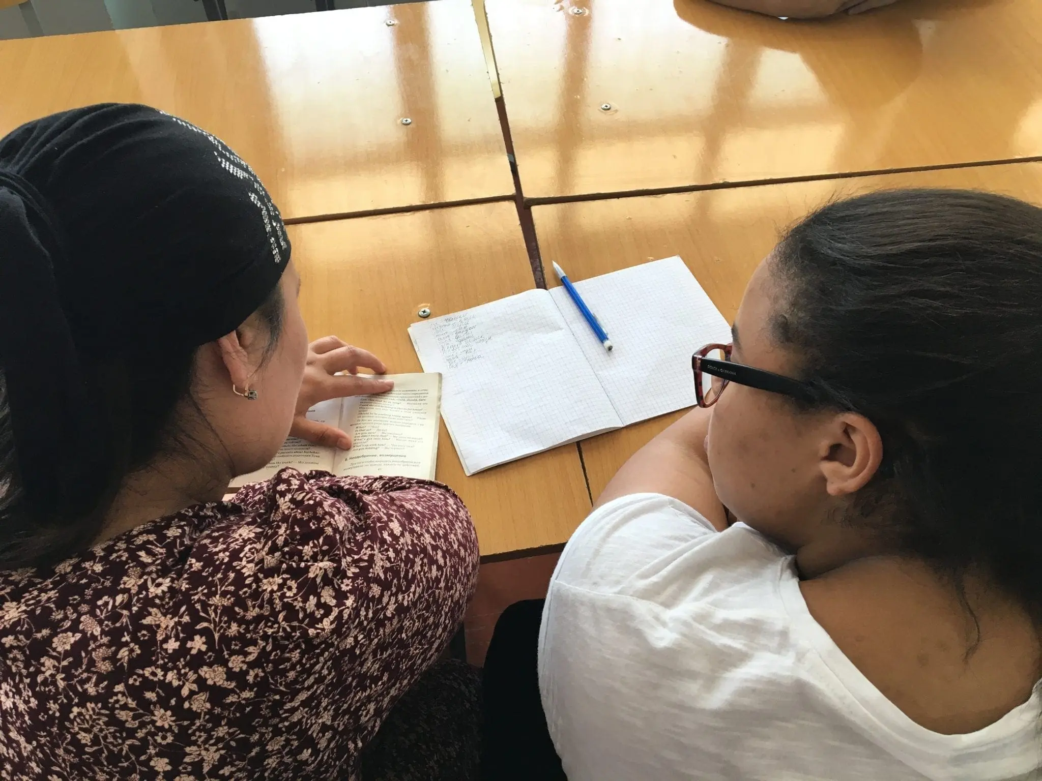 Two people sit at a table with a notebook and pen between them.