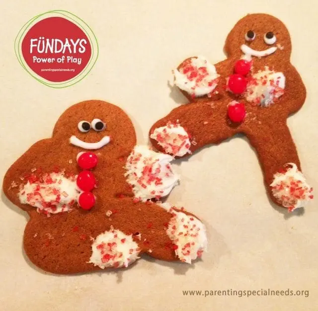 Two gingerbread men decorated with white icing, red candies, and crushed candy pieces.