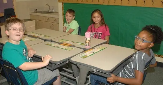 Four children sit at desks in a classroom.