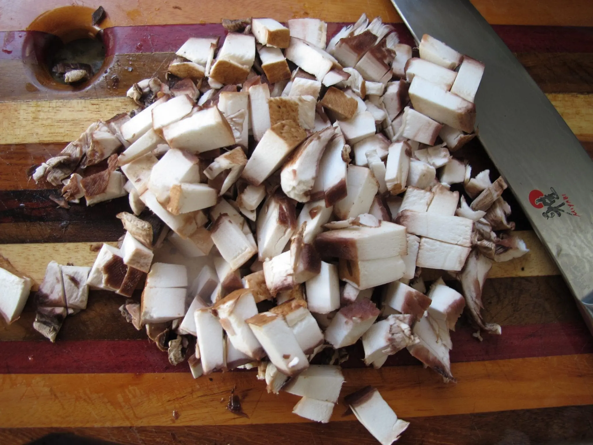 Pile of diced mushrooms on a cutting board next to a knife.