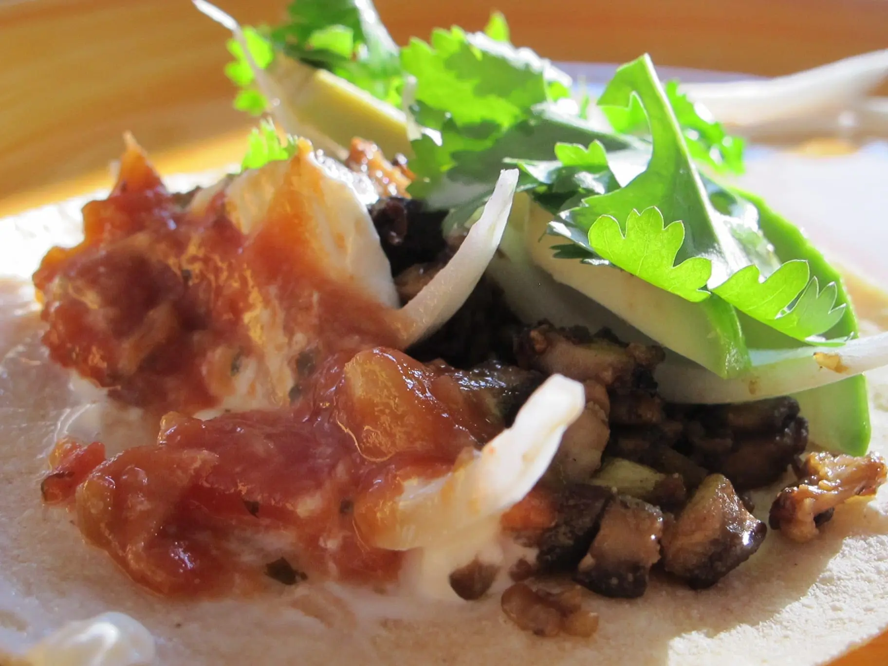 Mushroom taco with avocado, cilantro, and onion on a corn tortilla.