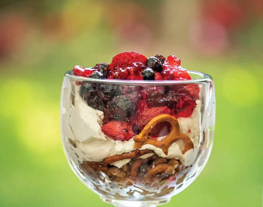 Festive Pretzel Salad with berries and whipped topping in a glass goblet.