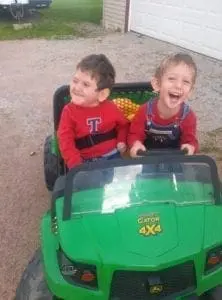 Two young boys smiling in a green toy Gator 4x4.