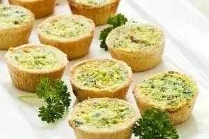 A plate of many mini bite-size quiche appetizers with parsley garnish