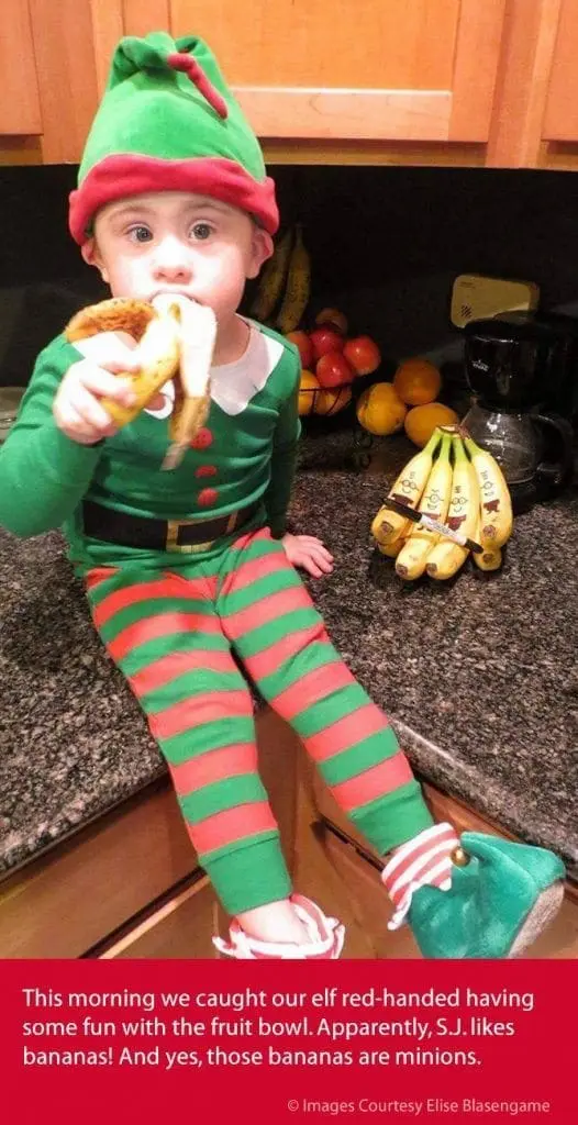 A young boy in an elf costume eats a banana.