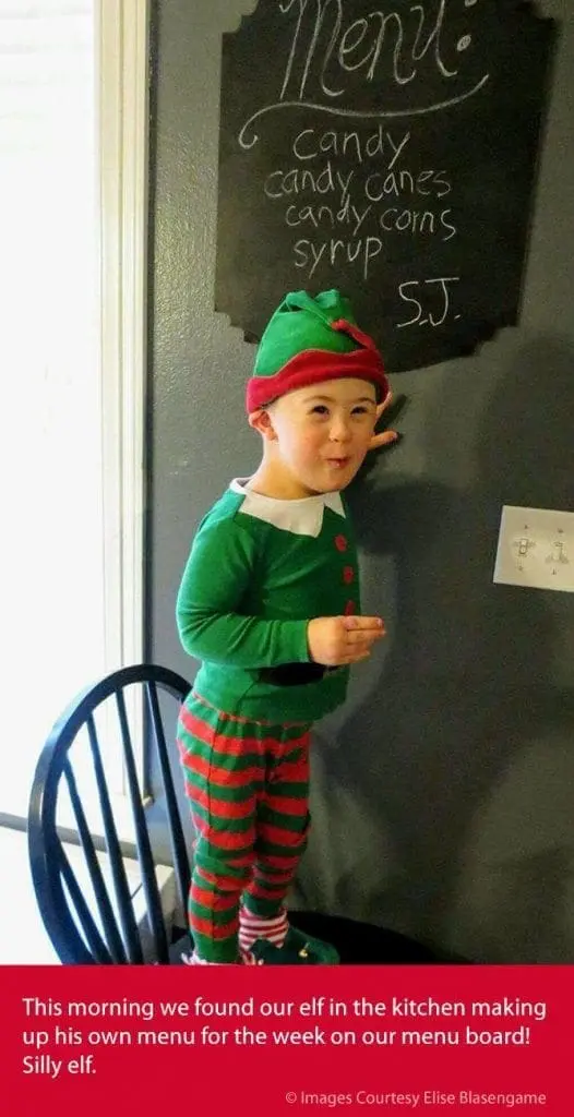 S.J. in an elf costume points to a menu board in the kitchen.
