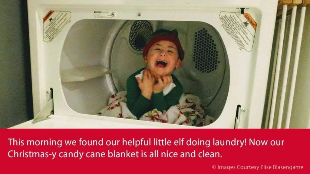 A child in an elf hat sits in a dryer, laughing.