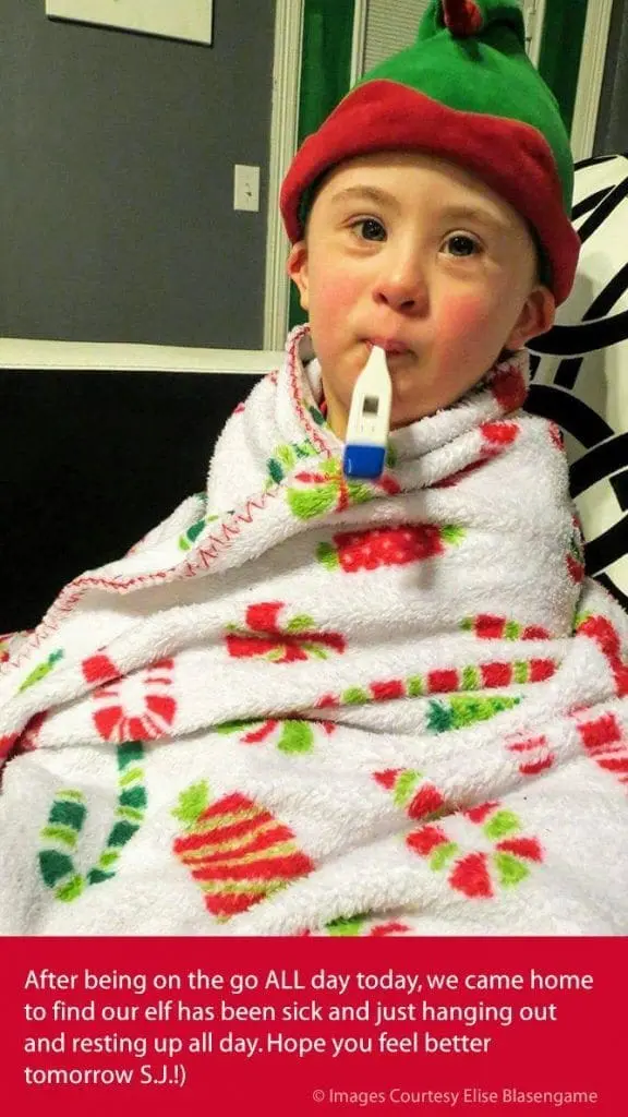 Child with Down syndrome wearing an elf hat and a thermometer in his mouth, wrapped in a festive blanket.